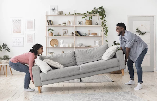 Black couple moving a sofa in their home. Both people seem to be having a good time.