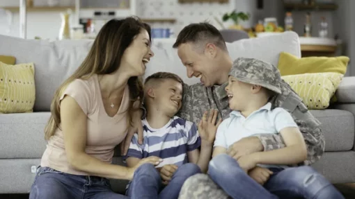 Soldier sitting in front of a couch with his wife and kids.