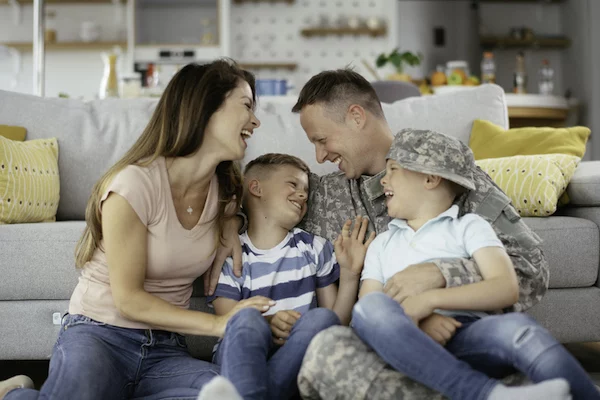 Soldier sitting in front of a couch with his wife and kids.