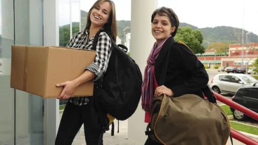 Two smiling students walking toward a building with a cardboard box