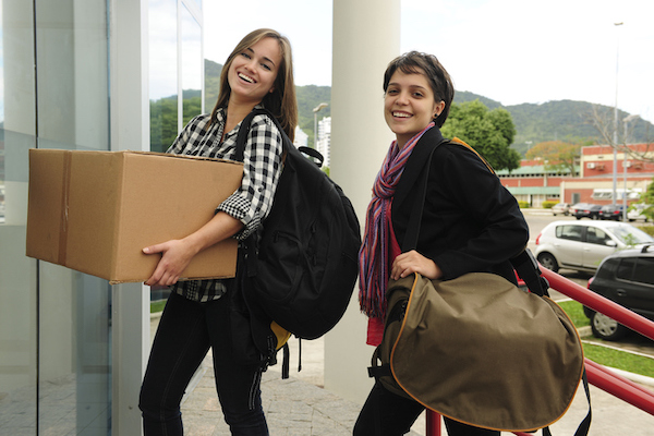 Two smiling students walking toward a building with a cardboard box