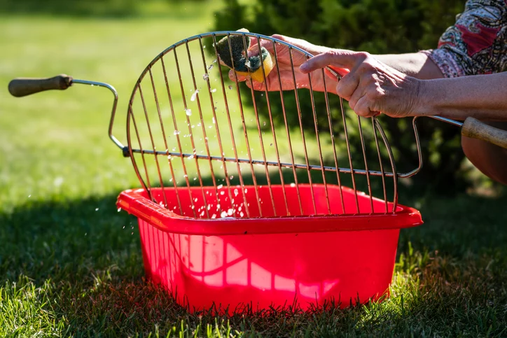 woman cleaning grates of a charcoal grill with soap and water