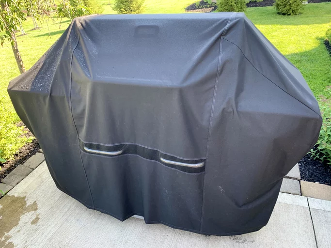 grill with black cover on cement padio, green grass in background