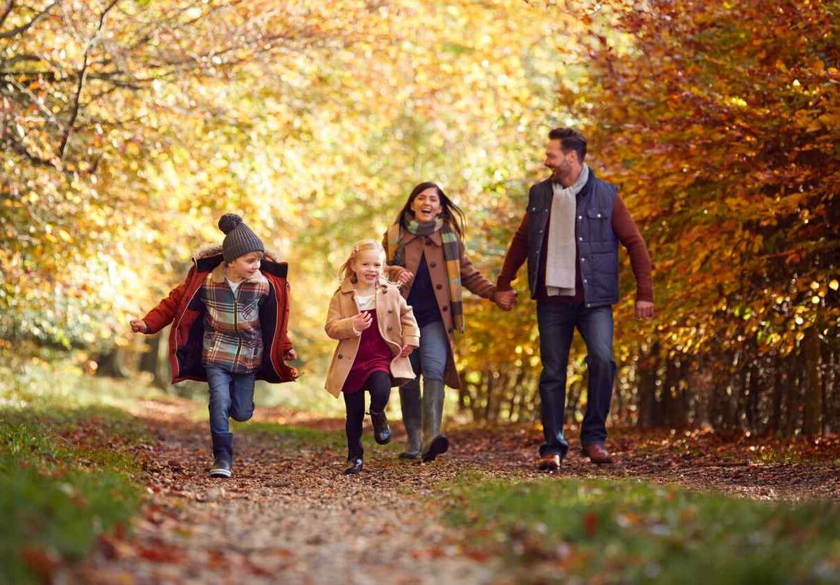 A family walks outdoors on a path surrounded by fall leaves