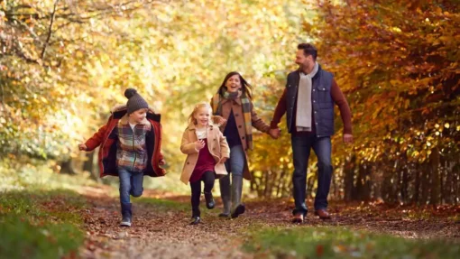 A family walks outdoors on a path surrounded by fall leaves