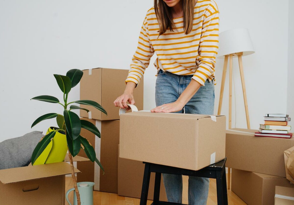 A woman packs up a living room and tapes a box closed.