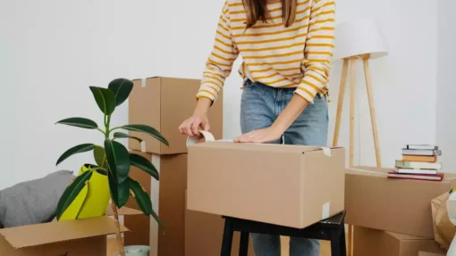 A woman packs up a living room and tapes a box closed.