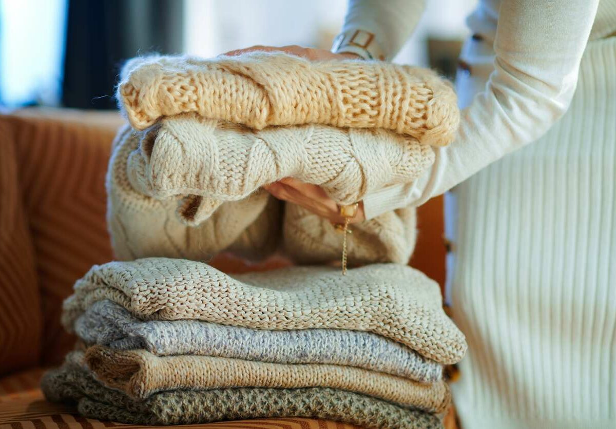 A woman folds and stacks cream and brown colored sweaters.