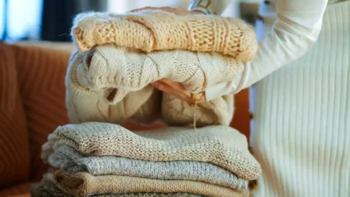 A woman folds and stacks cream and brown colored sweaters.