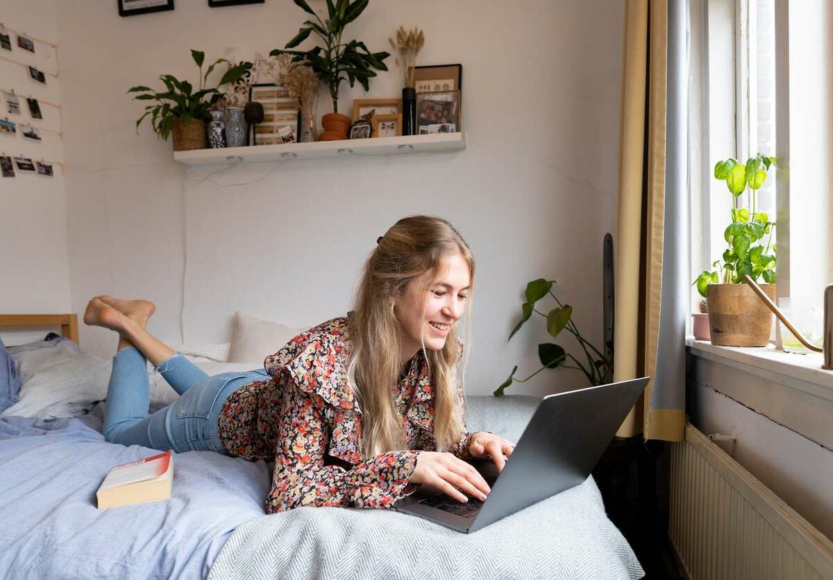 A woman lays on a bed and works on a laptop.