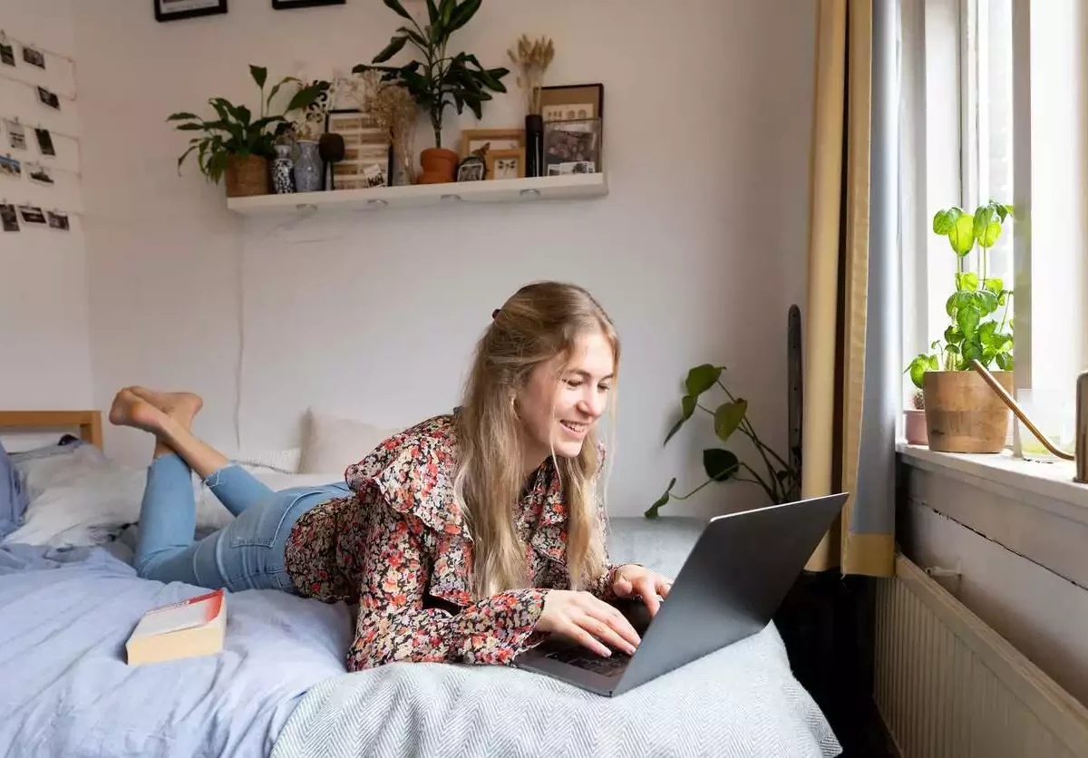 A woman lays on a bed and works on a laptop.