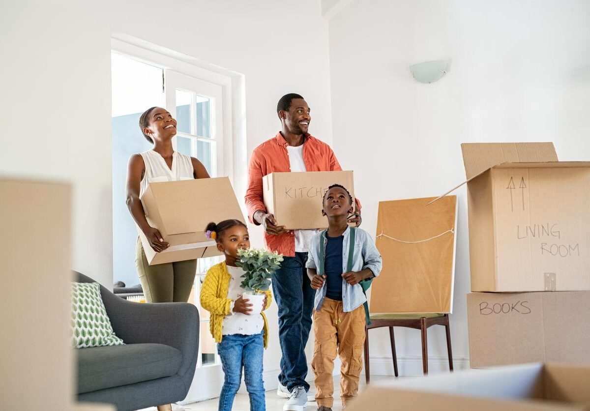 A family with two parents and children walks into a home carrying boxes