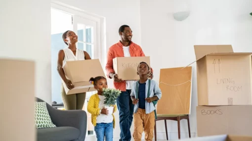 A family with two parents and children walks into a home carrying boxes