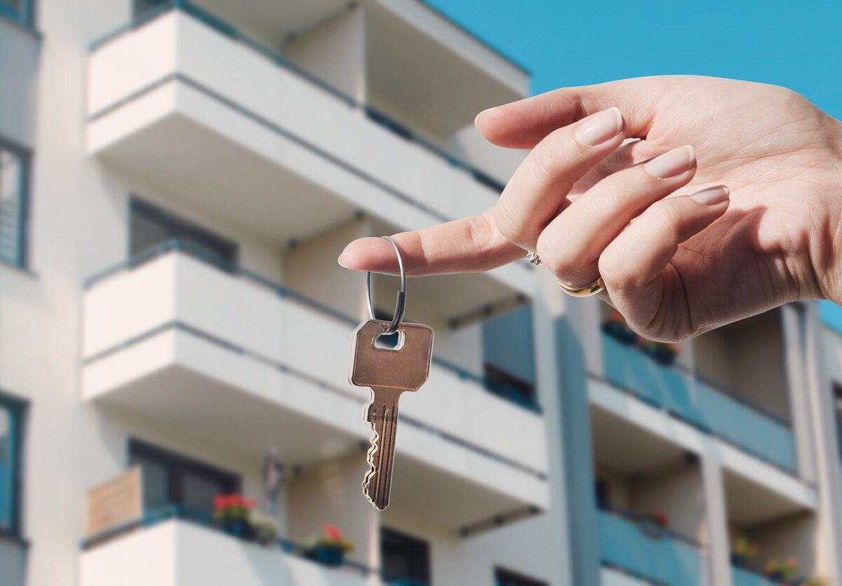 A person holds a key on a ring in front of a condo rental property