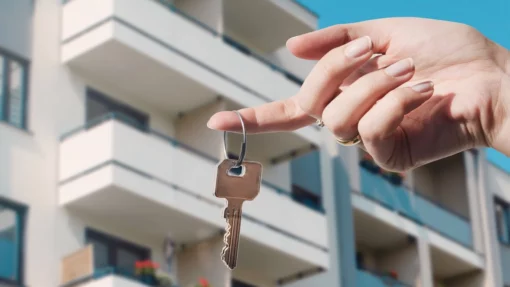 A person holds a key on a ring in front of a condo rental property