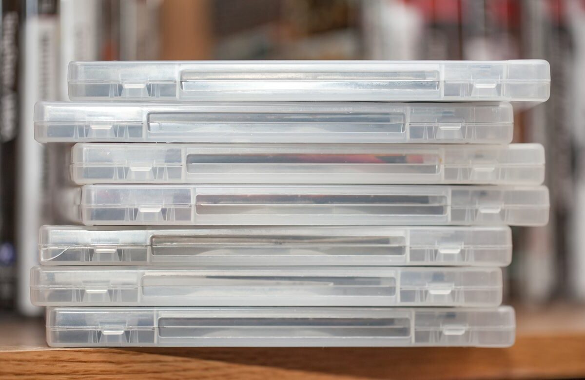 A stack of disks in clear cases sit on the edge of a shelf