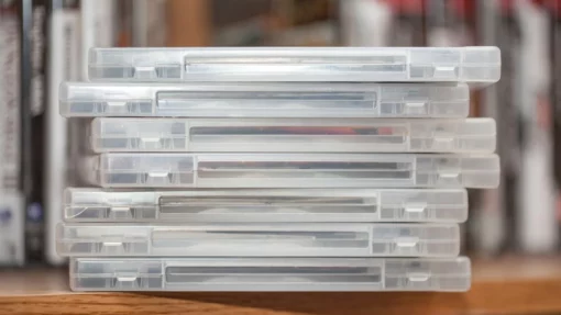 A stack of disks in clear cases sit on the edge of a shelf