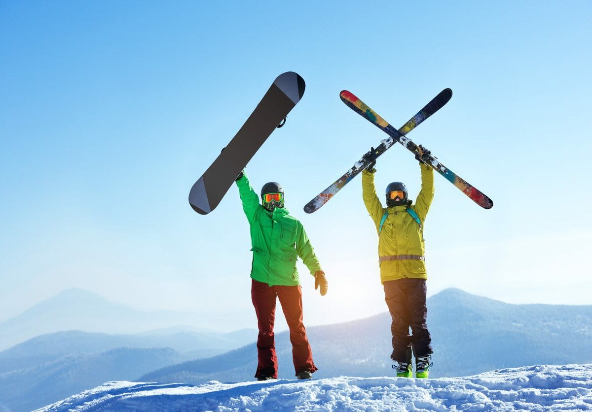 Two men holding a ski and snowboard at the top of a mountain.