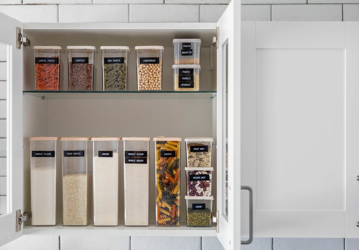 An open cabinet shows small, medium, and large clear plastic containers filled with dry food and labeled on the front
