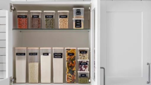 An open cabinet shows small, medium, and large clear plastic containers filled with dry food and labeled on the front