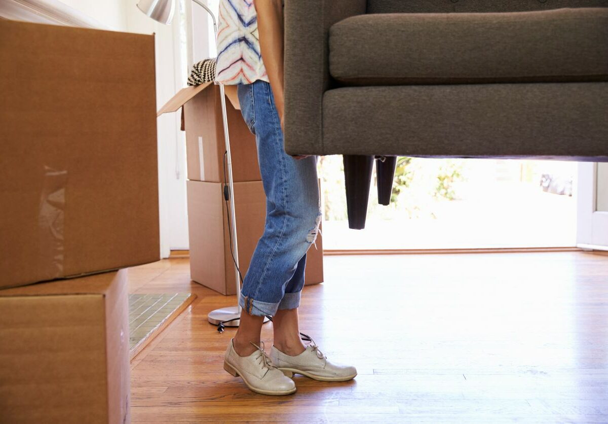 A woman carries a gray couch during the moving process.