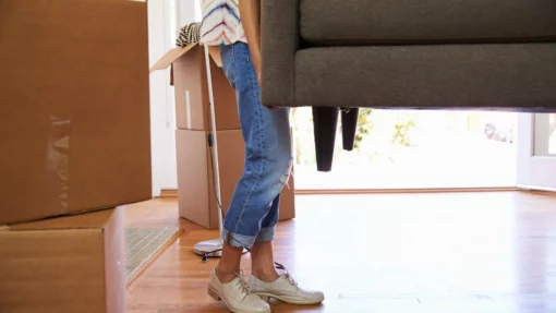 A woman carries a gray couch during the moving process.