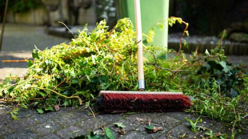 A red broom with a wooden handle sits among a pile of greenery that has been swept up.
