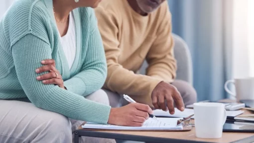 A man and woman sit on a couch and talk while filling out paperwork