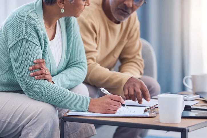 A man and woman sit on a couch and talk while filling out paperwork