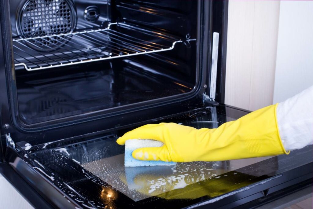 Person with glove and sponge in hand cleaning their oven.