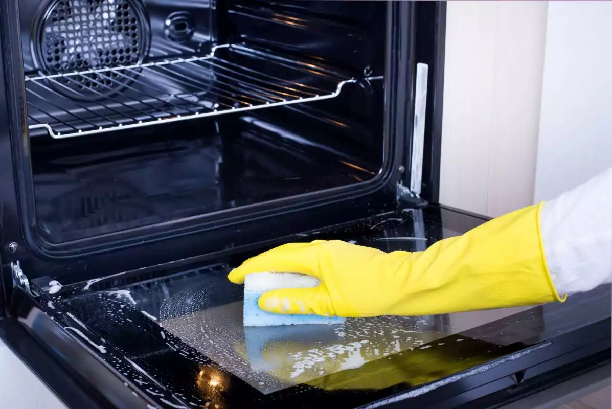 Person with glove and sponge in hand cleaning their oven.