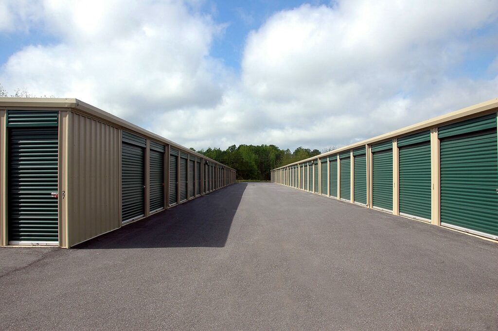 Two rows of outdoor storage units with green doors on a partly cloudy day.