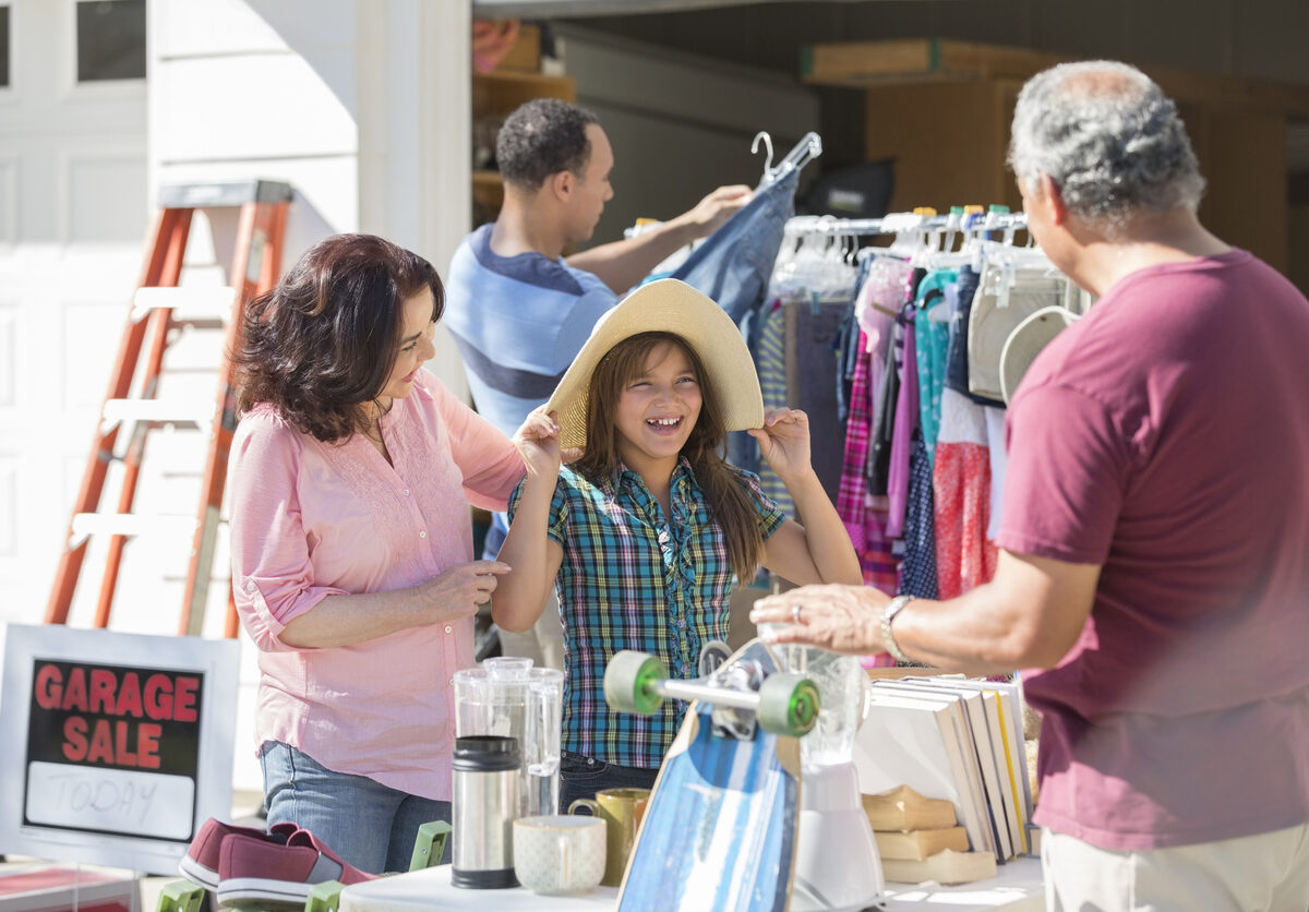 A mother and daughter trying on a floppy hat and shopping at a summer garage sale.