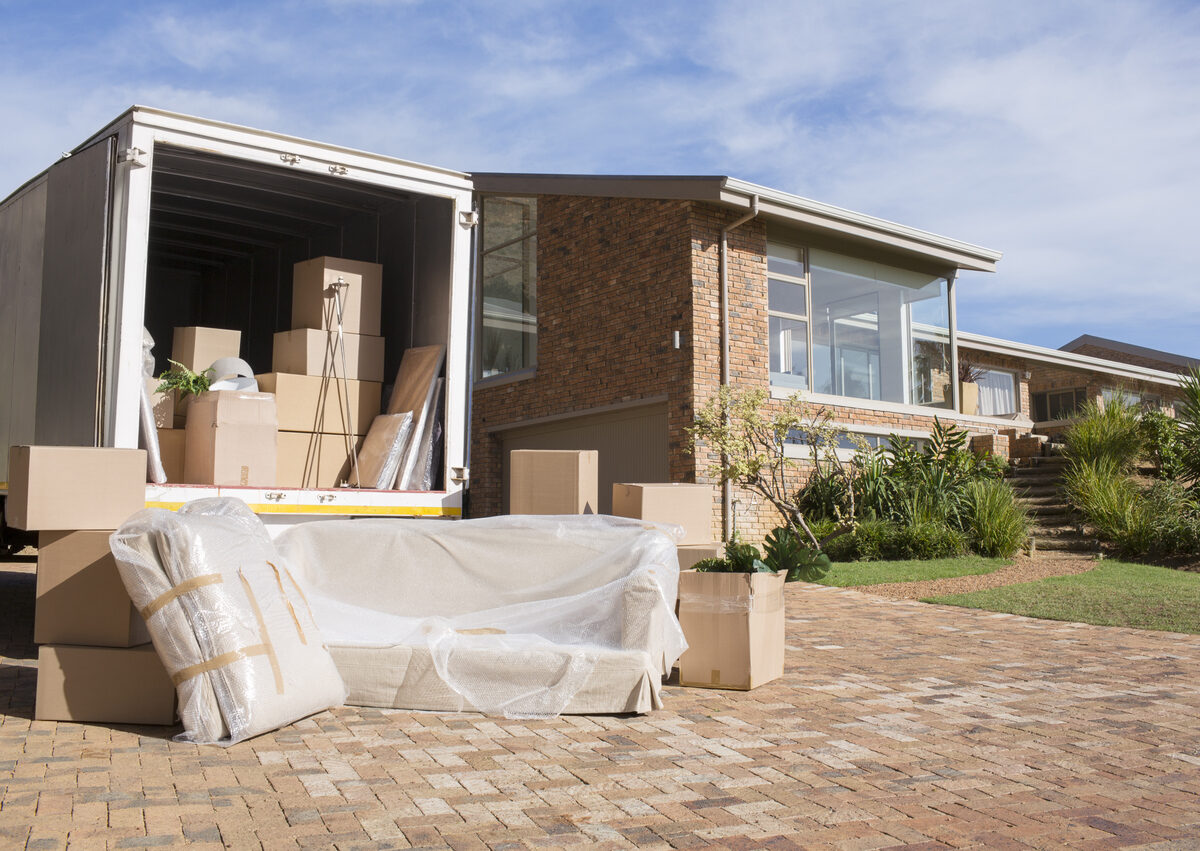 A moving truck in front of a house with various furniture pieces and boxes spilling out on a summer day.