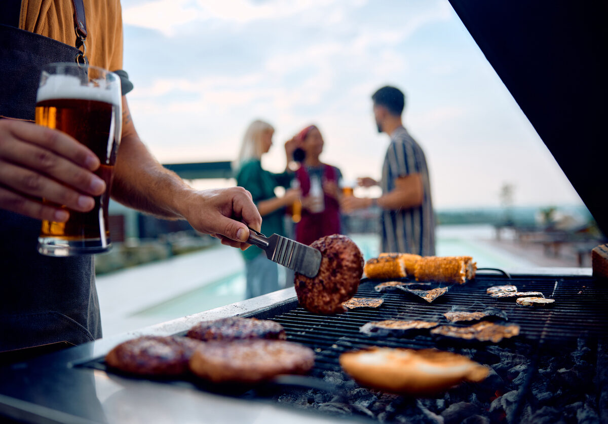 A close-up of a man grilling meats and veggies on a poolside grill.