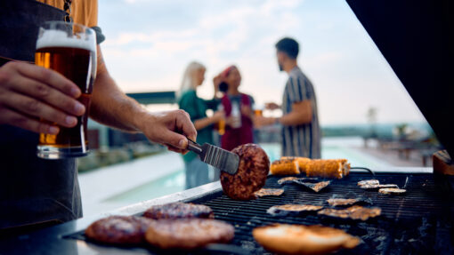 A close-up of a man grilling meats and veggies on a poolside grill.