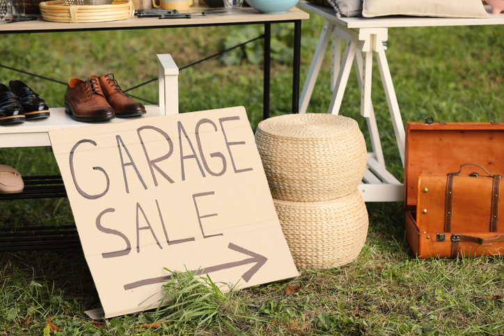 A cardboard sign reading “Garage Sale” pointing toward miscellaneous household items on grass.