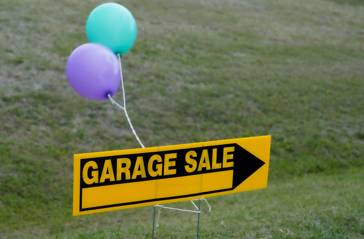 A yellow sign with an arrow that reads “garage sale” and a purple and blue balloon tied to the stakes.