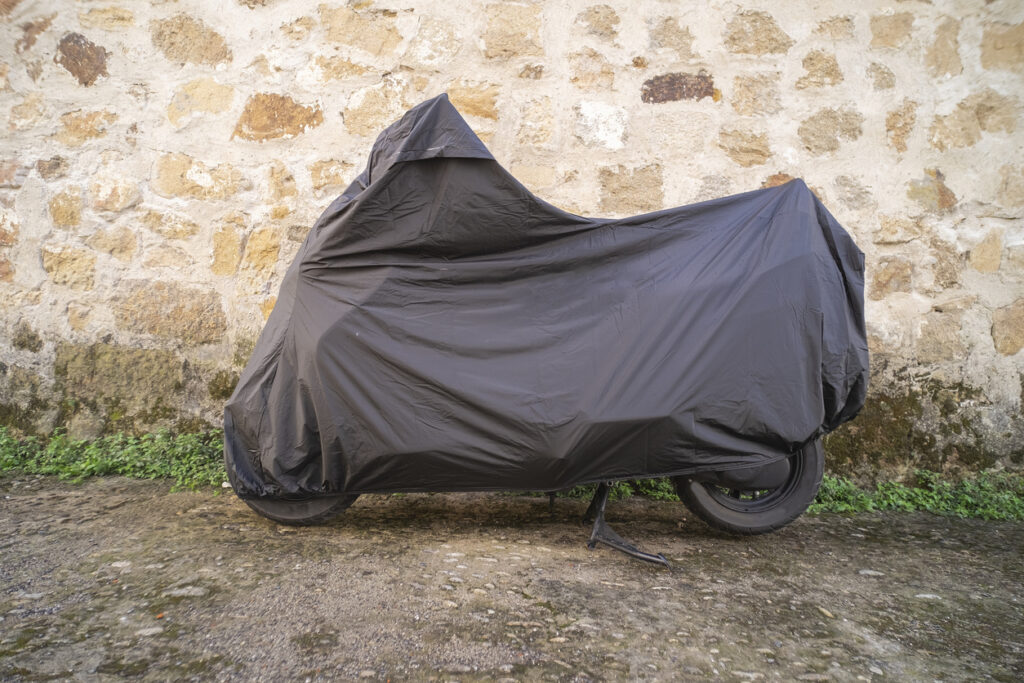  motorcycle with a black waterproof cover parked next to a stone wall.