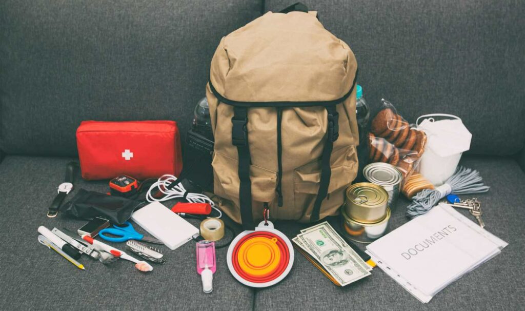 Items for a hurricane emergency kit, such as a first-aid kit, documents, and food, surround a backpack.