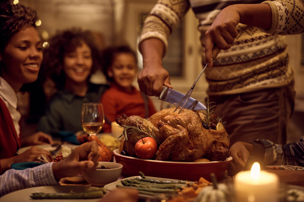 A father carves a Thanksgiving turkey as his family watches.