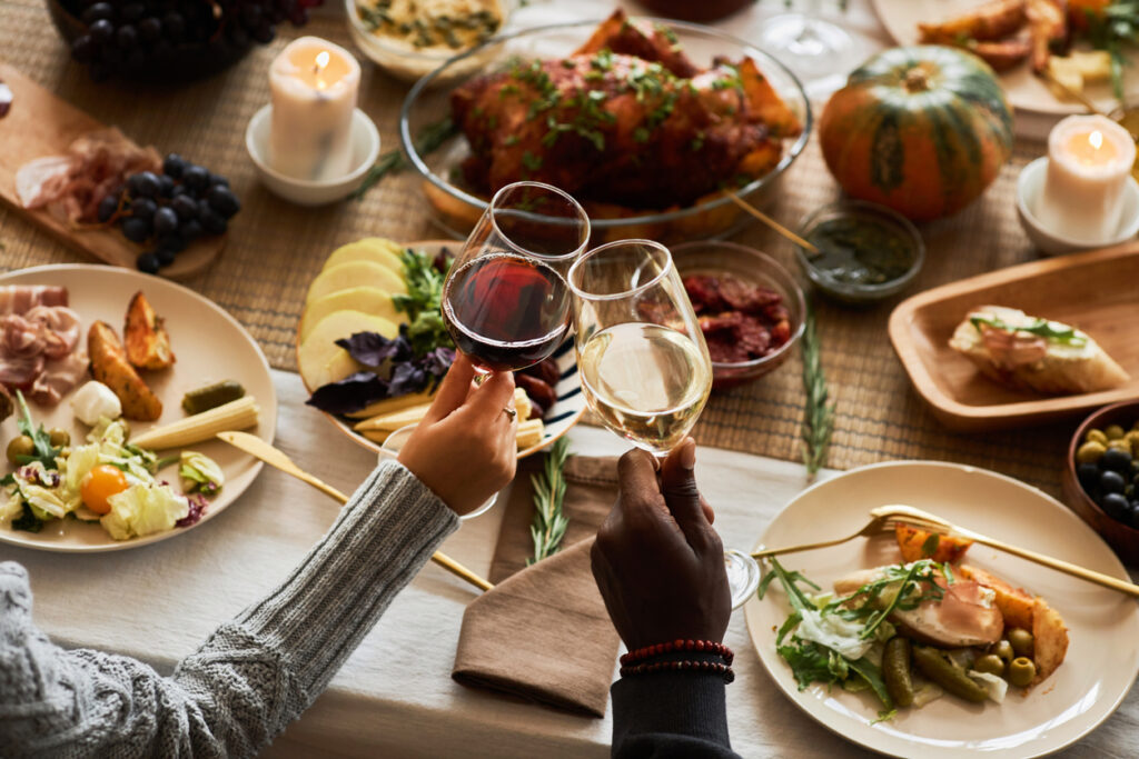 Two people toasting their wine glasses before a Thanksgiving dinner spread