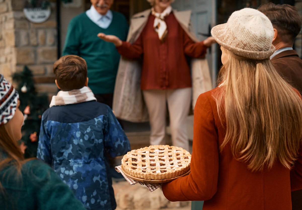 Grandparents greet their family as they arrive for Thanksgiving, holding a pie.