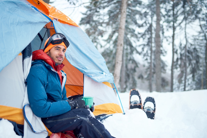 A man enjoys a cup of coffee in his properly packed winter camping tent.