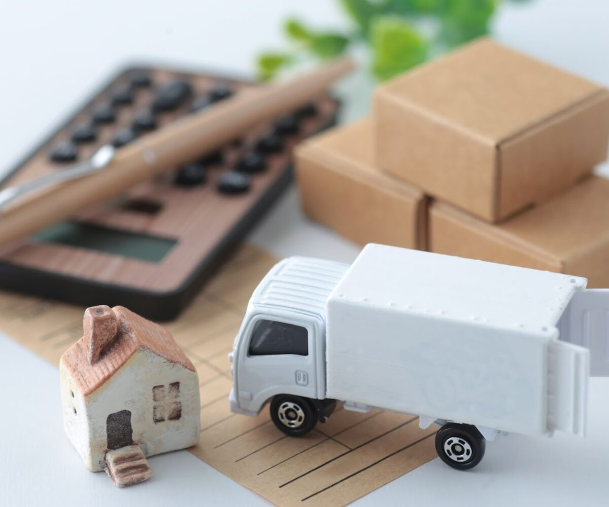 A miniature moving truck and home sit next to a wooden calculator.