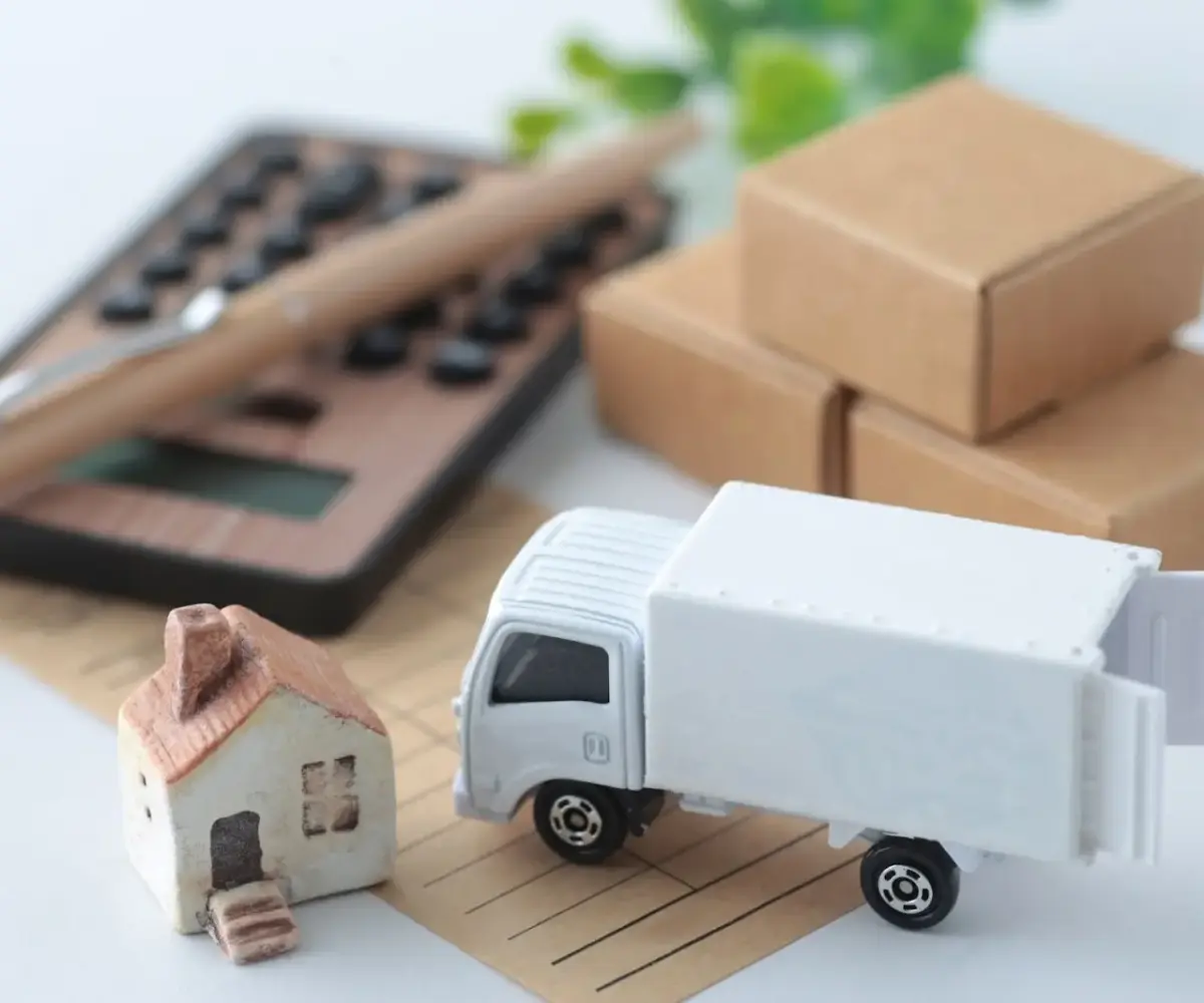 A miniature moving truck and home sit next to a wooden calculator.