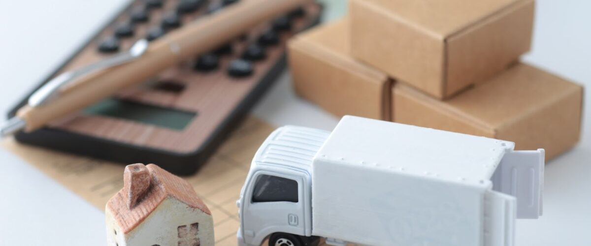A miniature moving truck and home sit next to a wooden calculator.