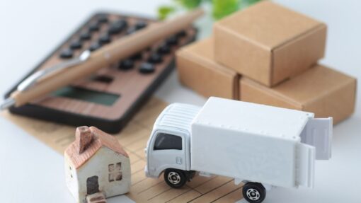 A miniature moving truck and home sit next to a wooden calculator.