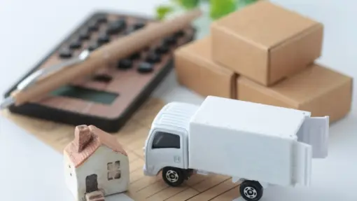 A miniature moving truck and home sit next to a wooden calculator.