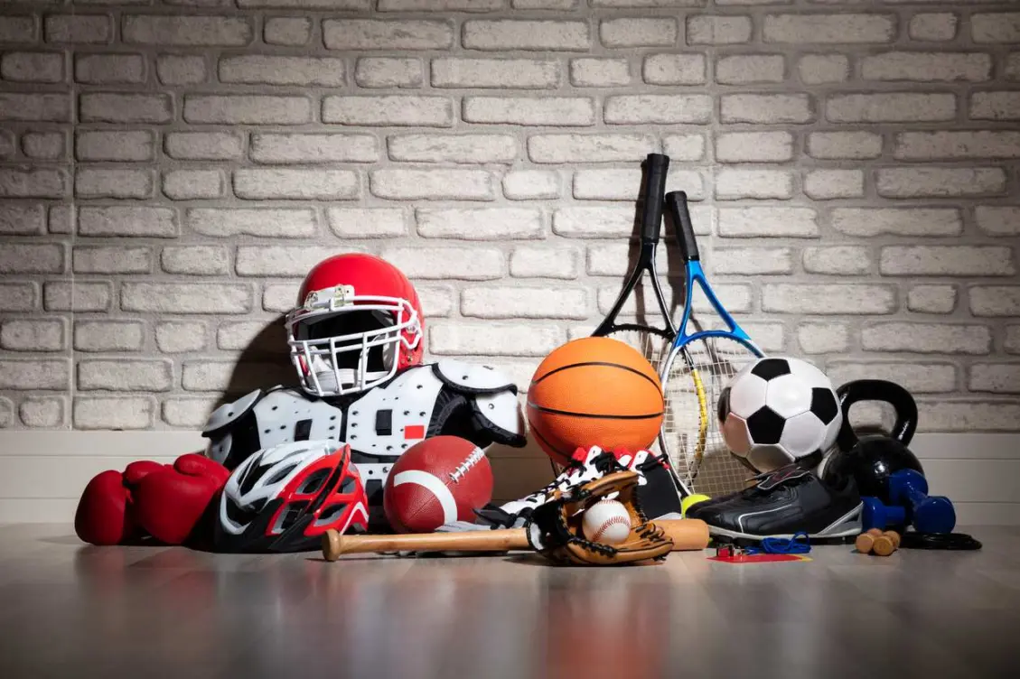 Sports gear arranged on the floor. There is a football, helmet, and basketball, among them.